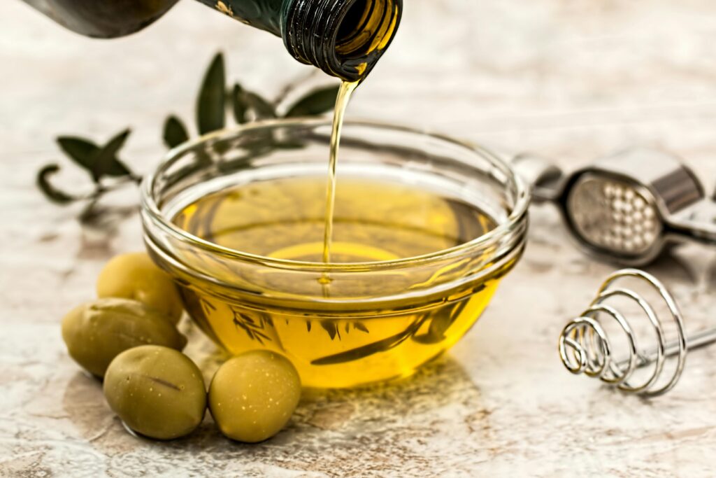 olive-oil-salad-dressing-cooking-olive-33783 Close-up of olive oil being poured into a glass bowl surrounded by fresh olives and kitchen tools.